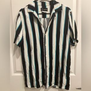Men’s short sleeve button up with black/white/blue/pink vertical stripe pattern.